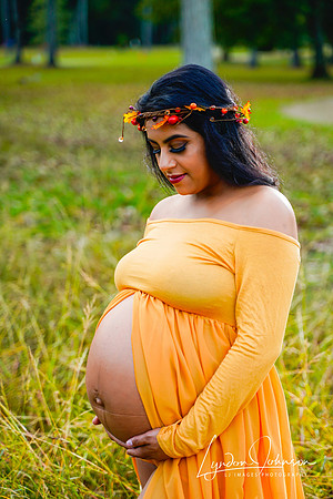 Outdoor maternity portrait in gold dress with belly showing, looking down at belly